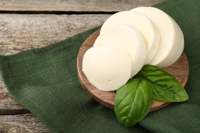 Photo of Board with tasty mozzarella slices and basil leaves on wooden table, closeup. Space for text