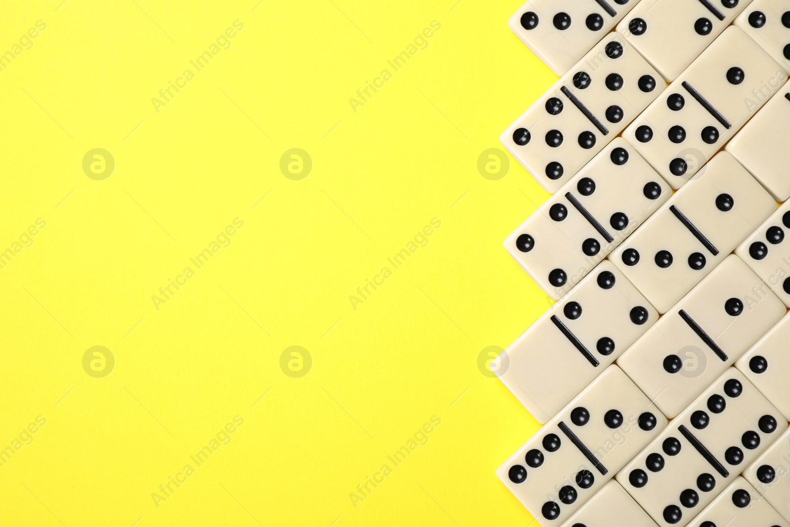 Photo of Classic domino tiles on yellow background, flat lay. Space for text