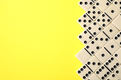 Photo of Classic domino tiles on yellow background, flat lay. Space for text