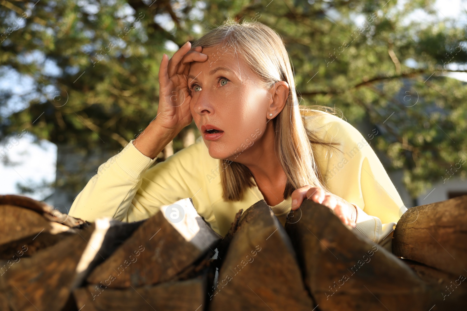 Photo of Concept of private life. Curious senior woman spying on neighbours over firewood outdoors