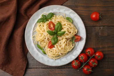 Delicious pasta with brie cheese, tomatoes and basil leaves on wooden table, flat lay