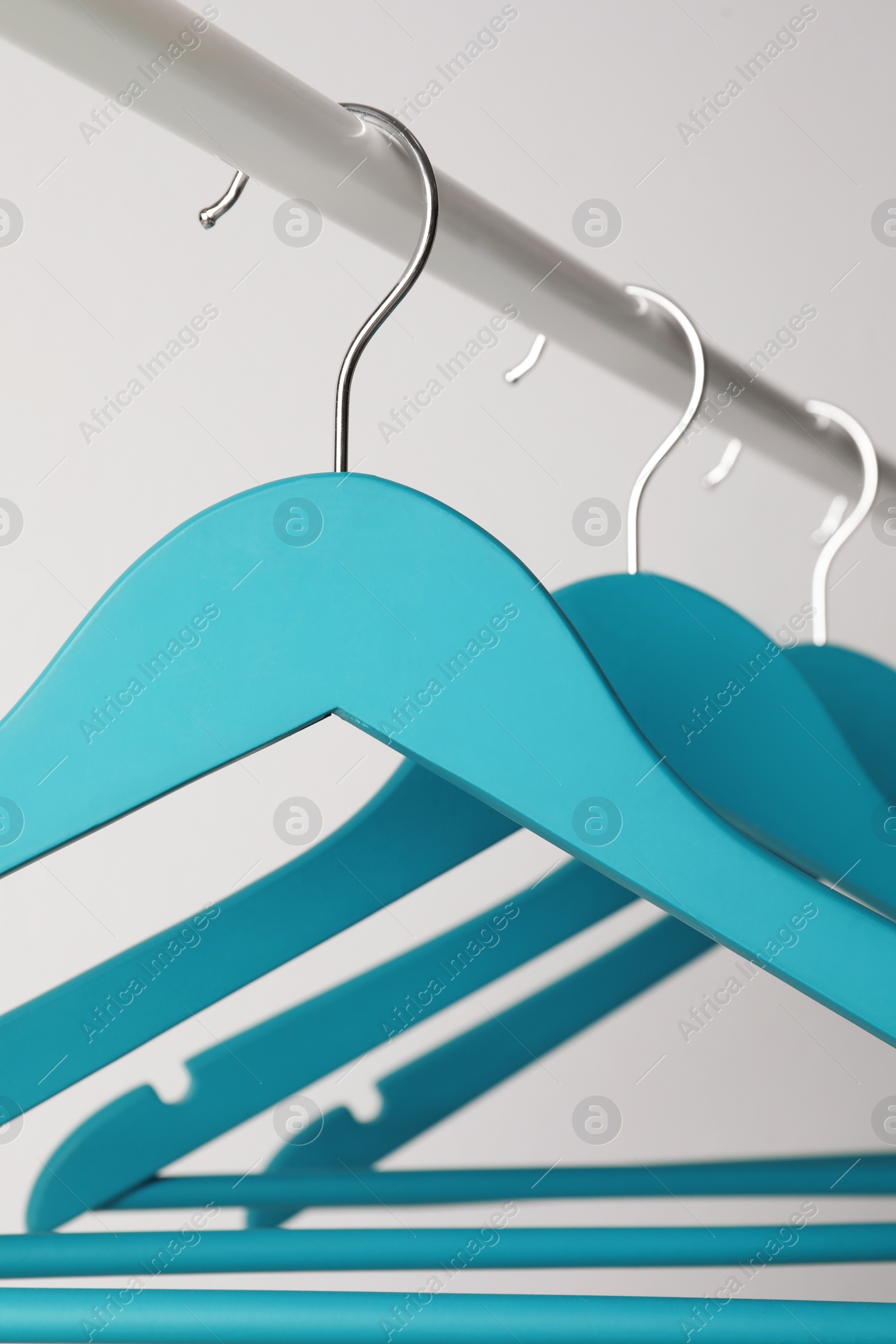 Photo of Empty turquoise clothes hangers on metal rail against light grey background, closeup