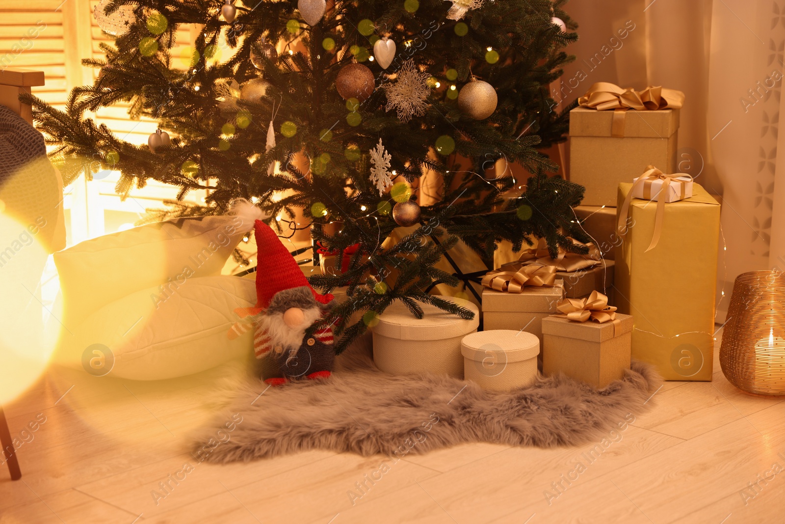 Photo of Christmas tree, gift boxes and gnome indoors. Bokeh effect