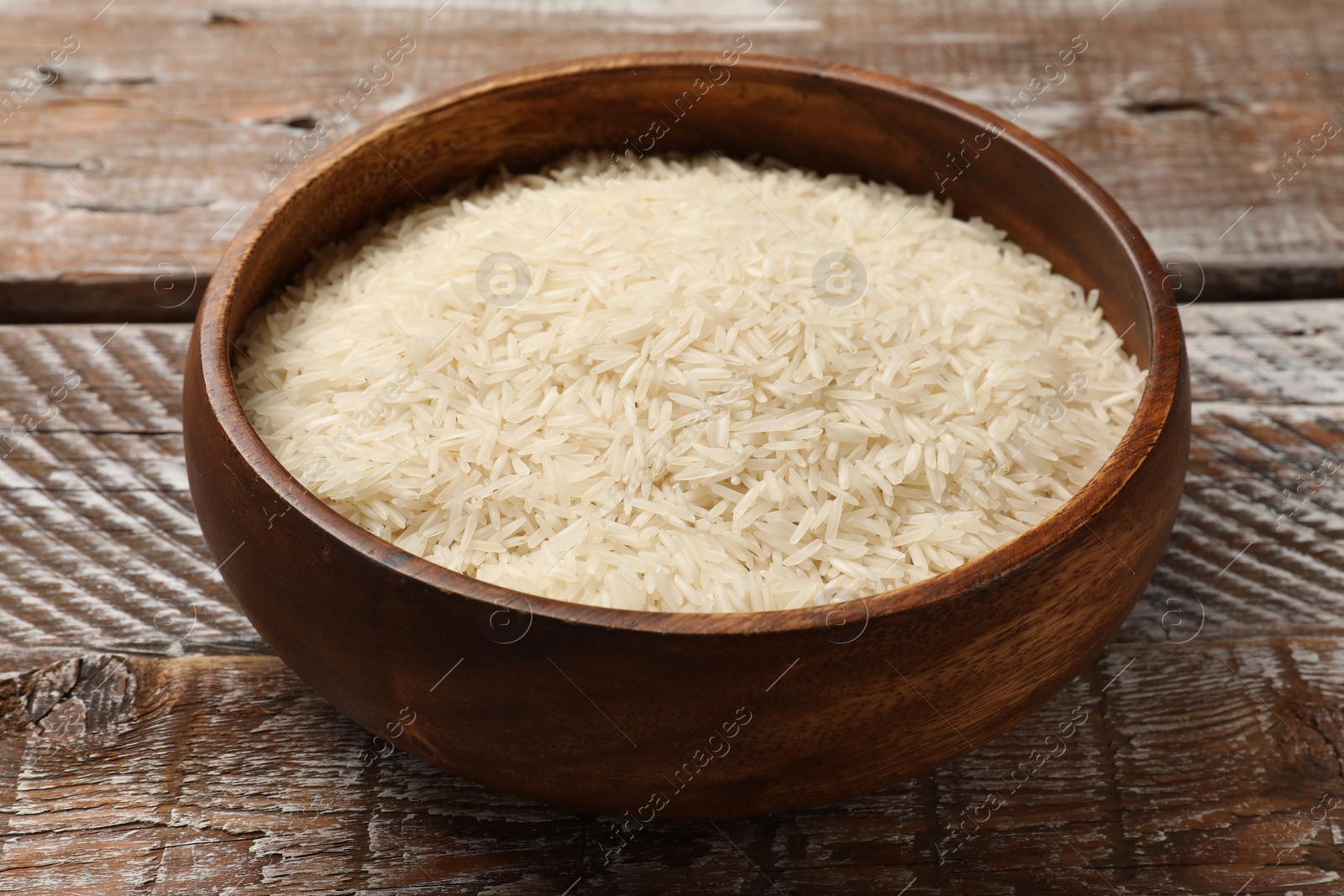 Photo of Raw basmati rice in bowl on wooden table, closeup