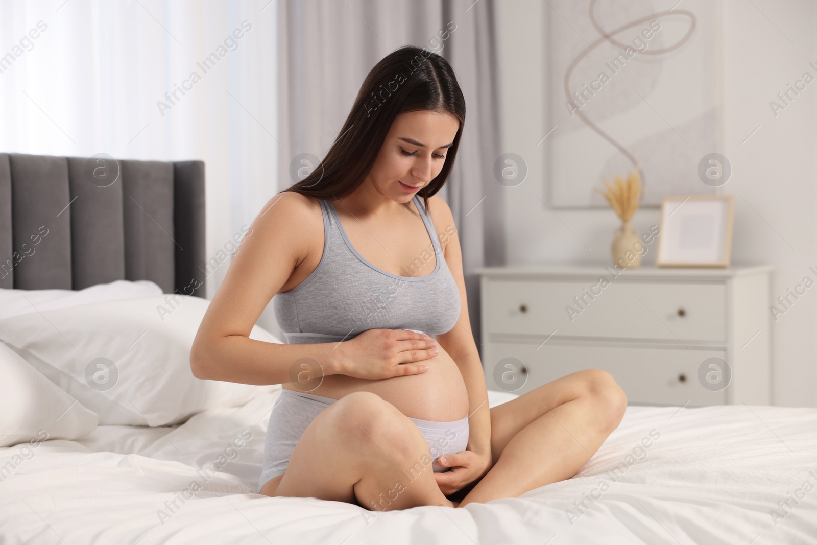 Photo of Beautiful pregnant woman in comfortable maternity underwear on bed at home