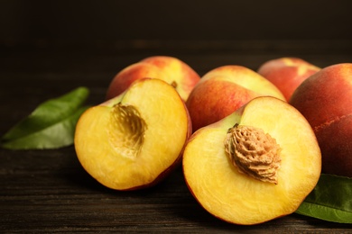 Photo of Fresh juicy peaches and leaves on black wooden table