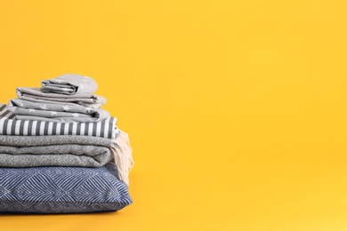 Stack of clean bed sheets and pillow on yellow background. Space for text