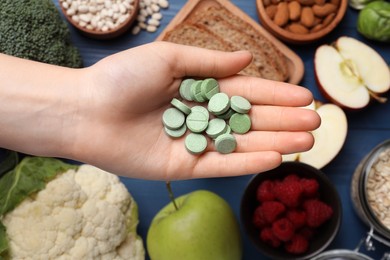 Photo of Woman holding pills at table with foodstuff, top view. Prebiotic supplements