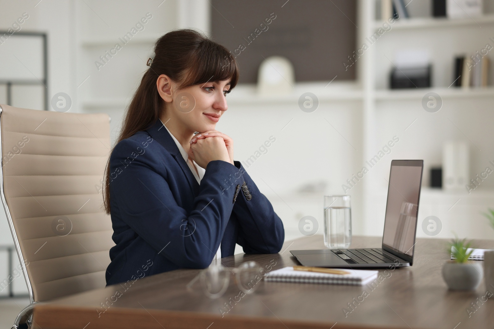 Photo of Woman watching webinar at wooden table in office