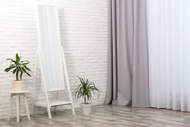 Modern interior with large mirror and dracaena plants near white brick wall