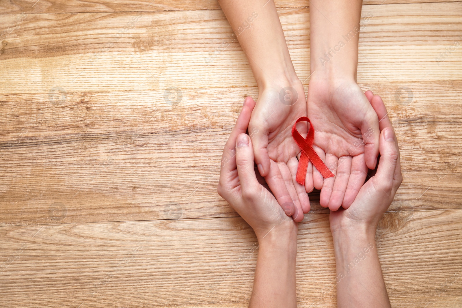 Photo of Women holding red awareness ribbon on wooden background, top view with space for text. World AIDS disease day