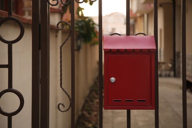 Red mailbox on metal fence outdoors, space for text