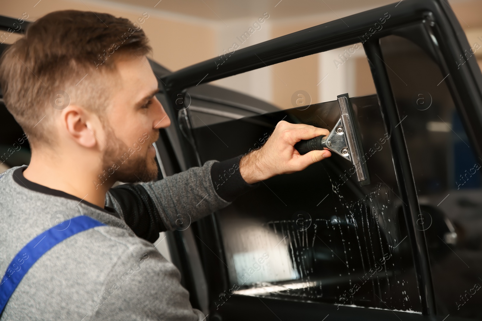 Photo of Skilled worker washing car window before tinting in shop