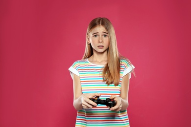 Teenage girl playing video games with controller on color background