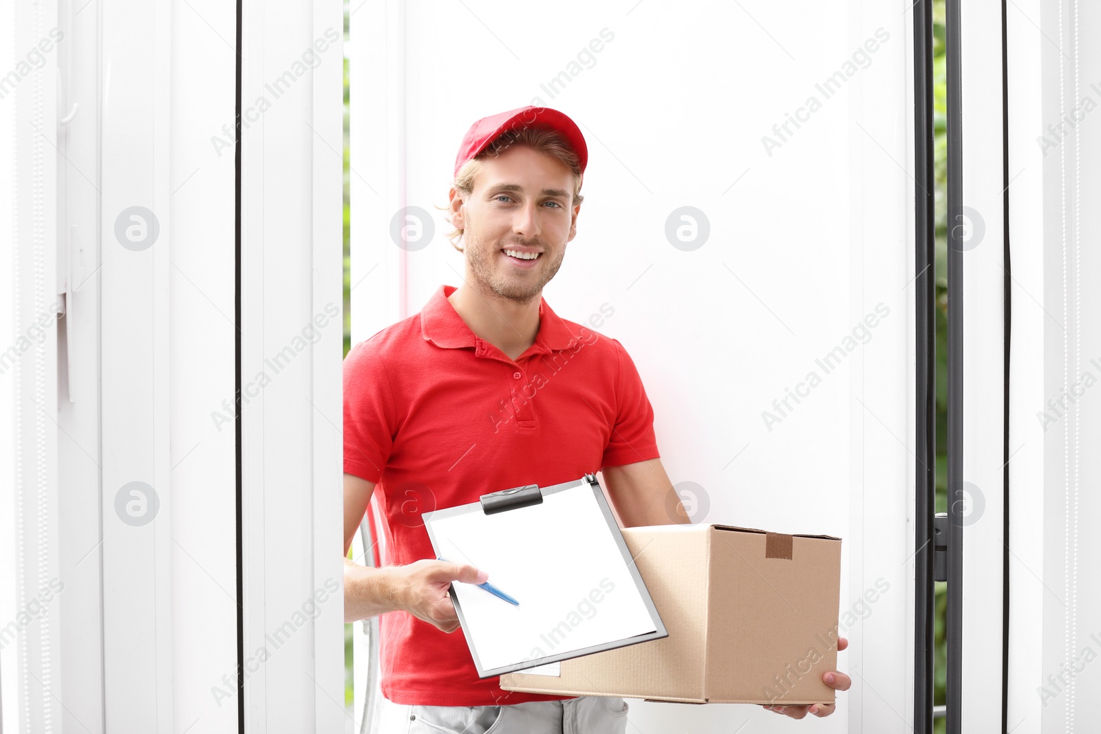 Photo of Young courier standing with parcel and clipboard on doorstep