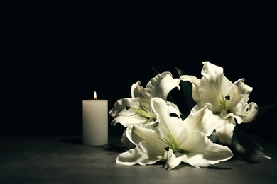 Photo of Beautiful lilies and burning candle on dark background with space for text. Funeral flowers