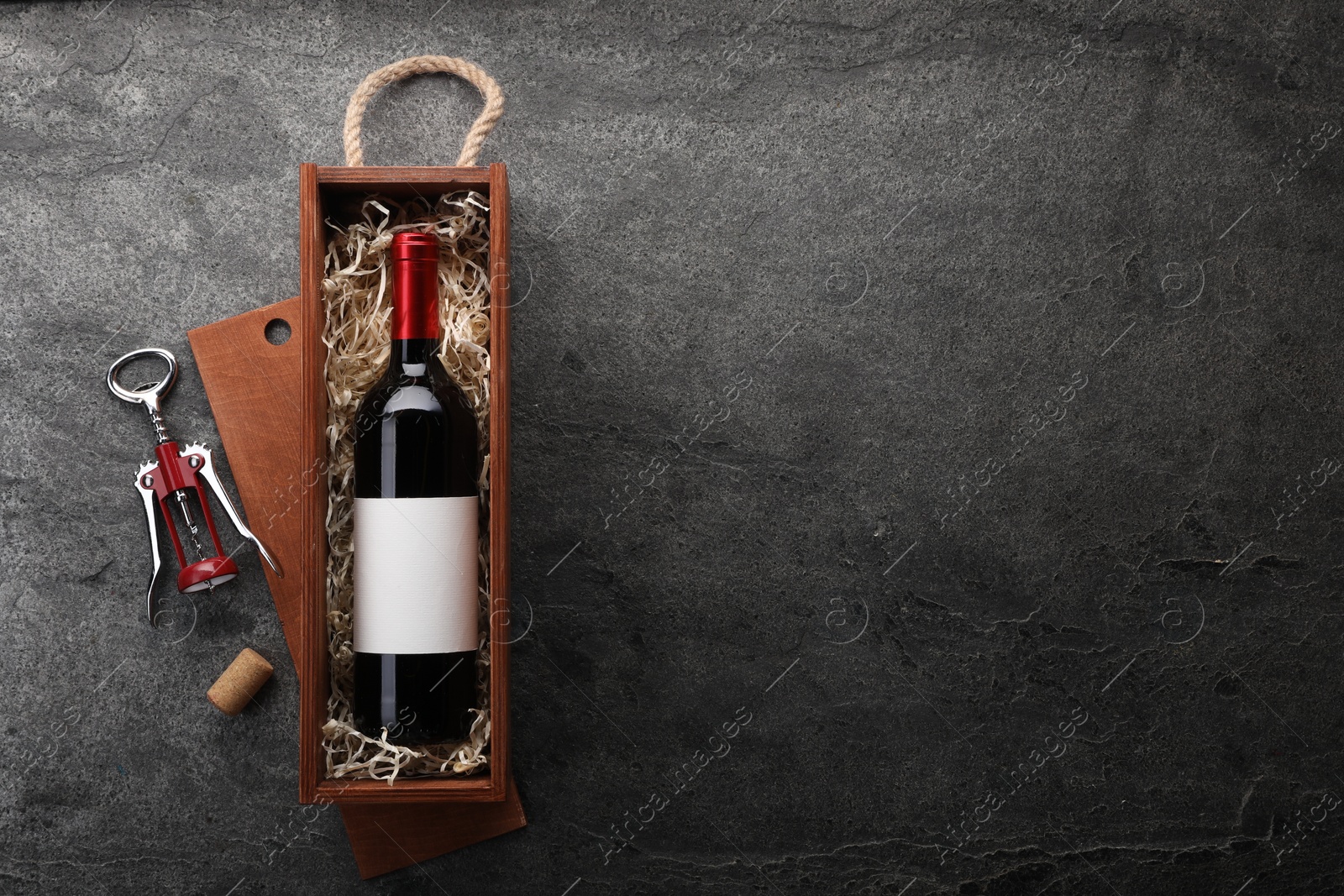 Photo of Bottle of wine in wooden box, cork and corkscrew on dark textured table, flat lay. Space for text