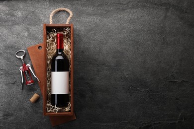 Bottle of wine in wooden box, cork and corkscrew on dark textured table, flat lay. Space for text