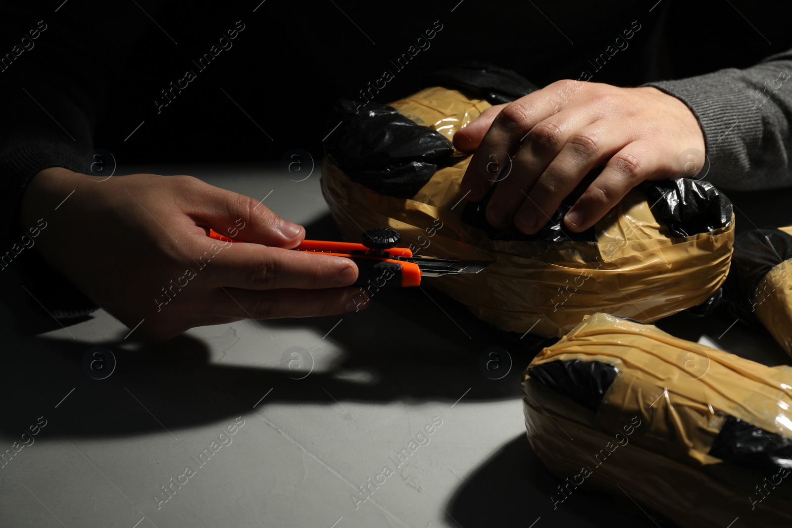 Photo of Smuggling and drug trafficking. Man opening package of narcotics with box cutter in darkness, closeup