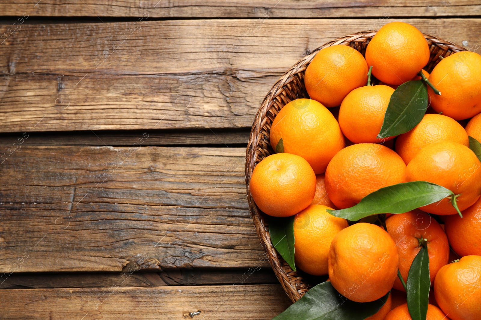 Photo of Fresh ripe tangerines with leaves and space for text on wooden table, top view. Citrus fruit