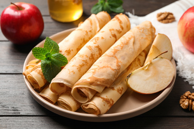 Photo of Delicious rolled thin pancakes on wooden table