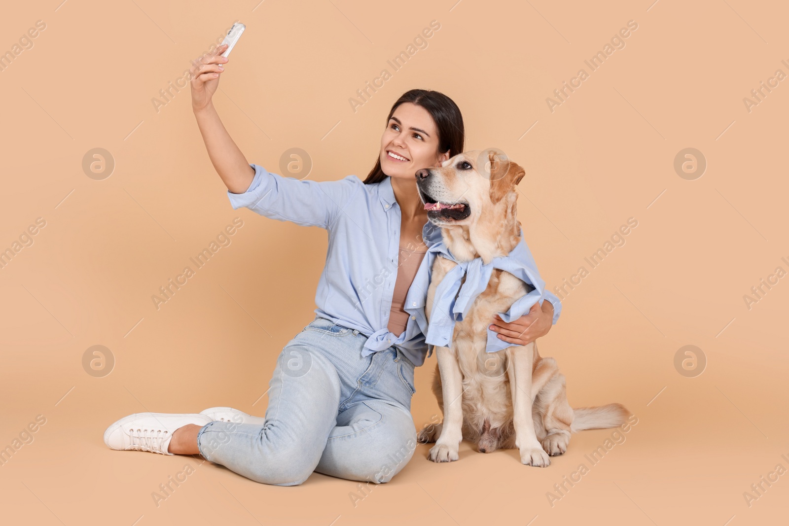Photo of Happy woman taking selfie with cute Labrador Retriever on beige background