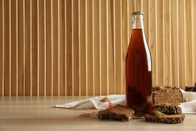 Photo of Bottle of delicious fresh kvass, spikelets and bread on wooden table. Space for text