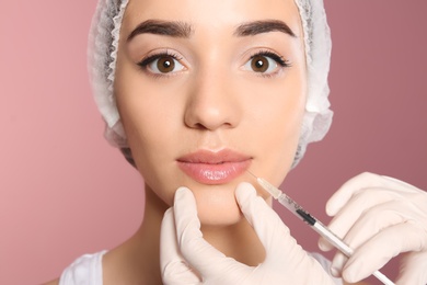 Photo of Young woman getting lip injection on color background