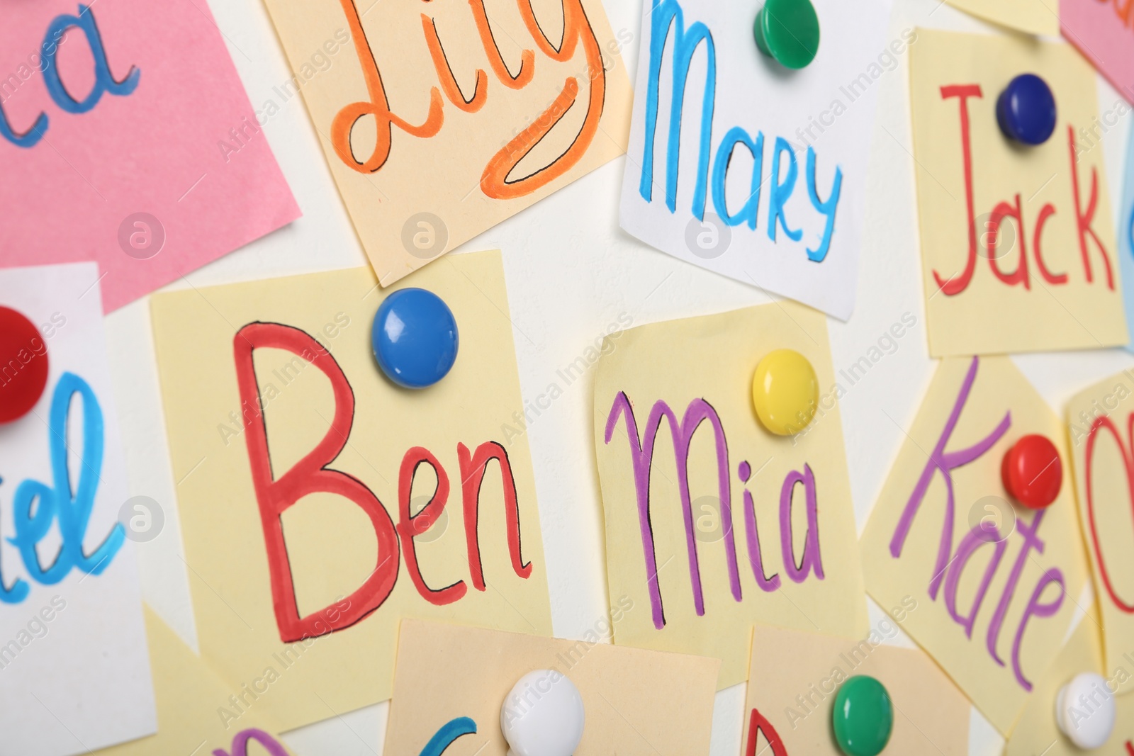 Photo of Colorful paper sheets with written different baby names on white background, closeup