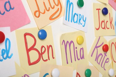 Colorful paper sheets with written different baby names on white background, closeup
