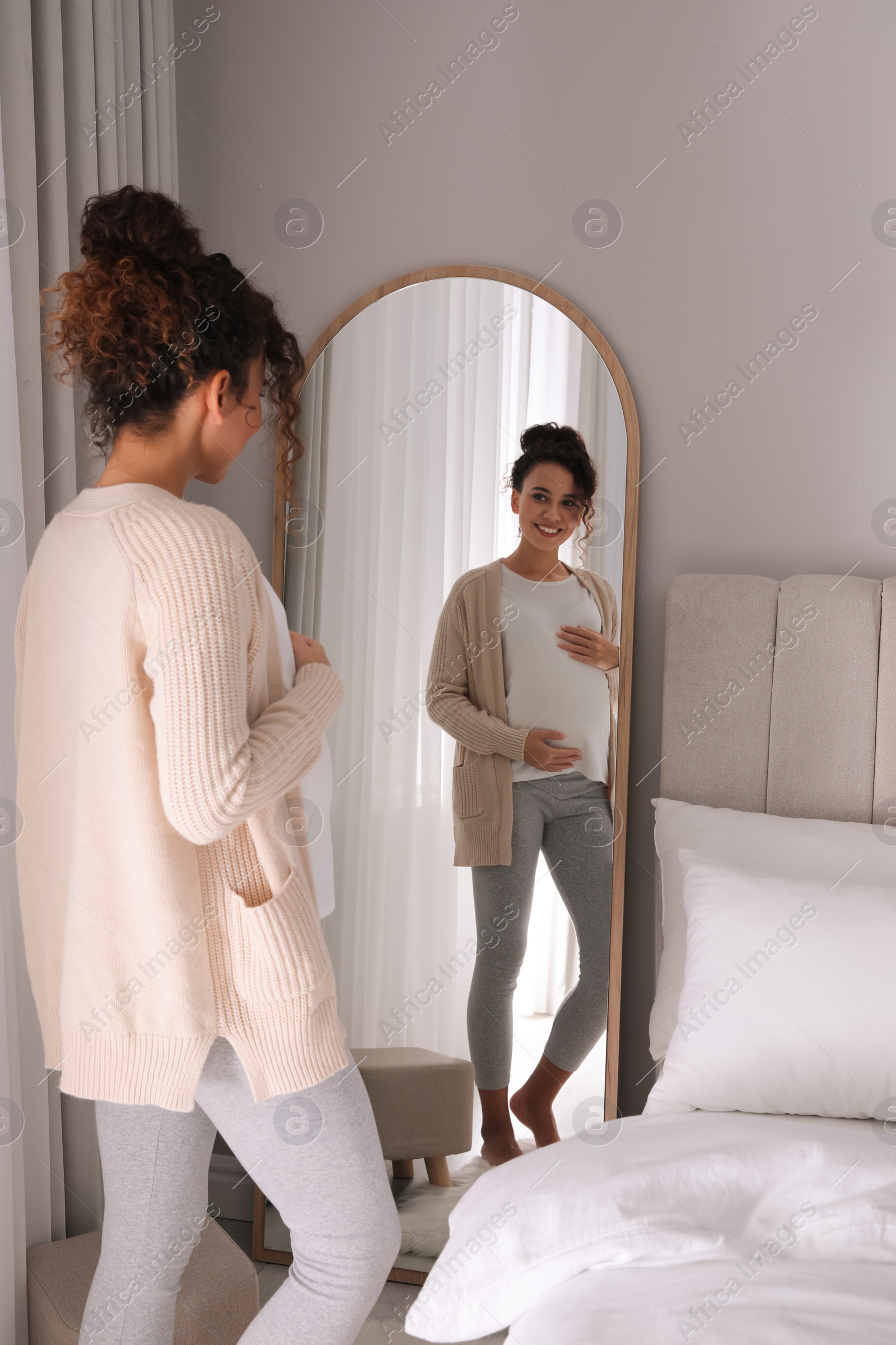 Photo of Pregnant young African-American woman near mirror at home