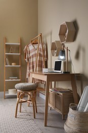 Photo of Comfortable wooden stool near table with laptop indoors. Interior design