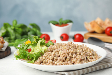 Tasty buckwheat porridge with salad on white wooden table. Space for text