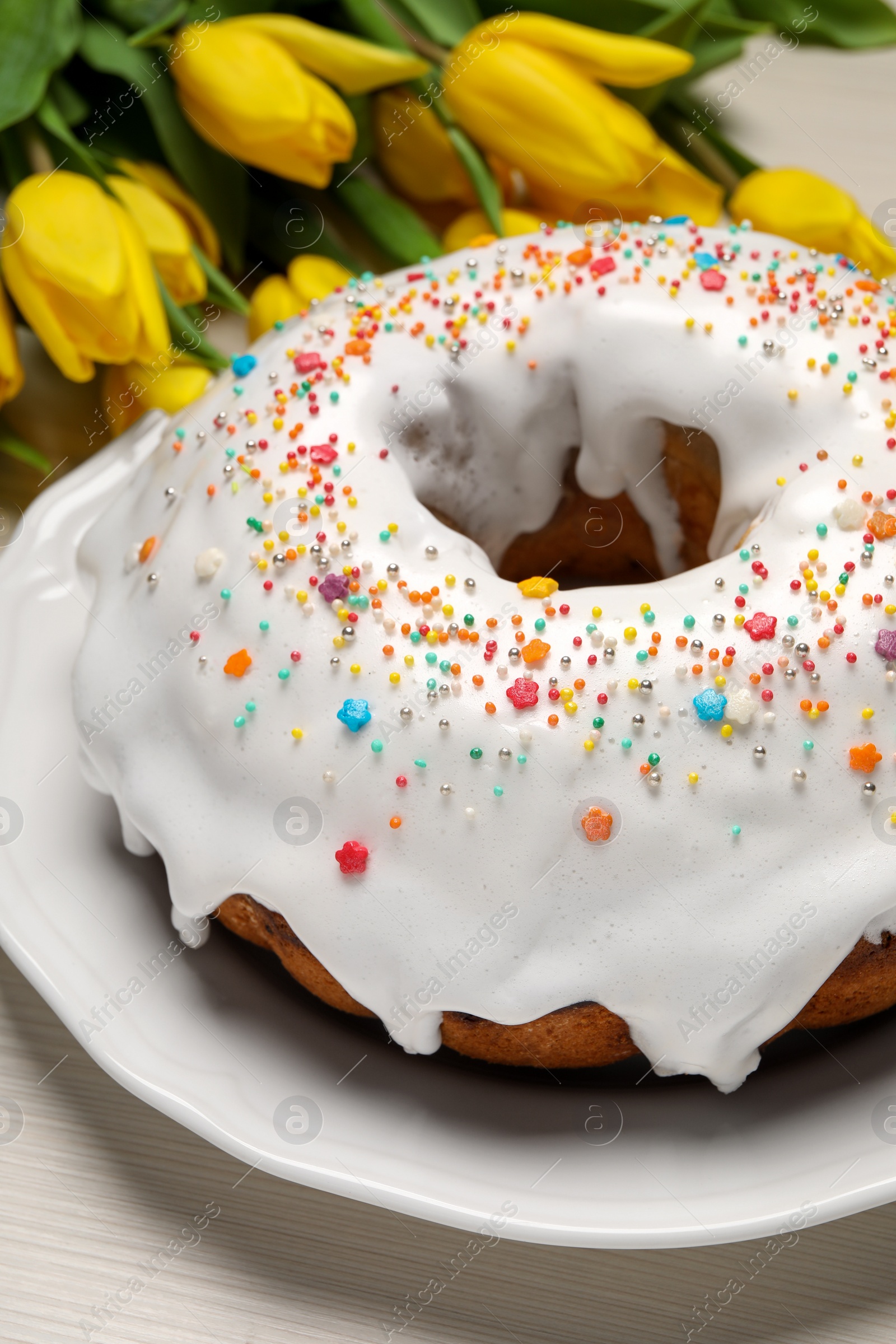 Photo of Easter cake with sprinkles and tulips on white wooden table, closeup