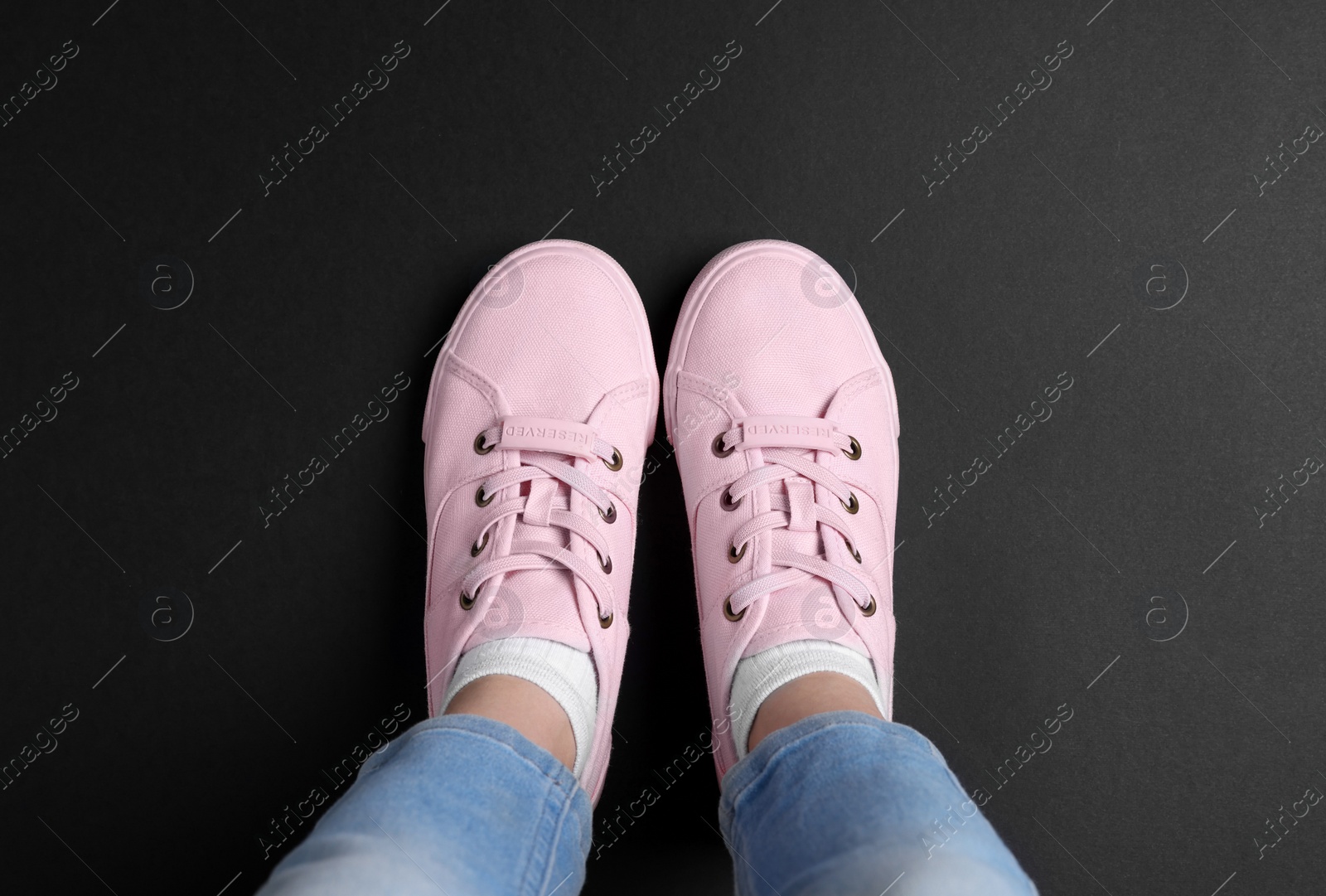 Photo of Woman in stylish sneakers standing on dark background, top view
