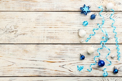 Shiny serpentine streamers and Christmas baubles on white wooden background, flat lay. Space for text