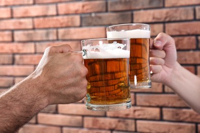 Photo of Friends clinking glasses of beer near red brick wall, closeup