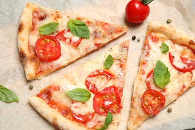 Photo of Slices of delicious pizza Margherita on parchment, flat lay