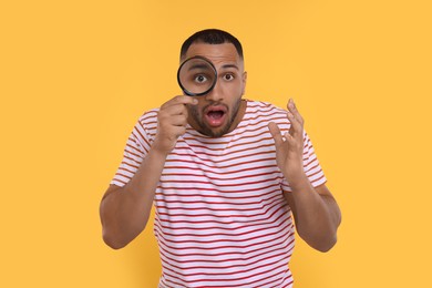 Shocked man looking through magnifier glass on orange background
