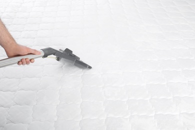 Man disinfecting mattress with vacuum cleaner, closeup. Space for text