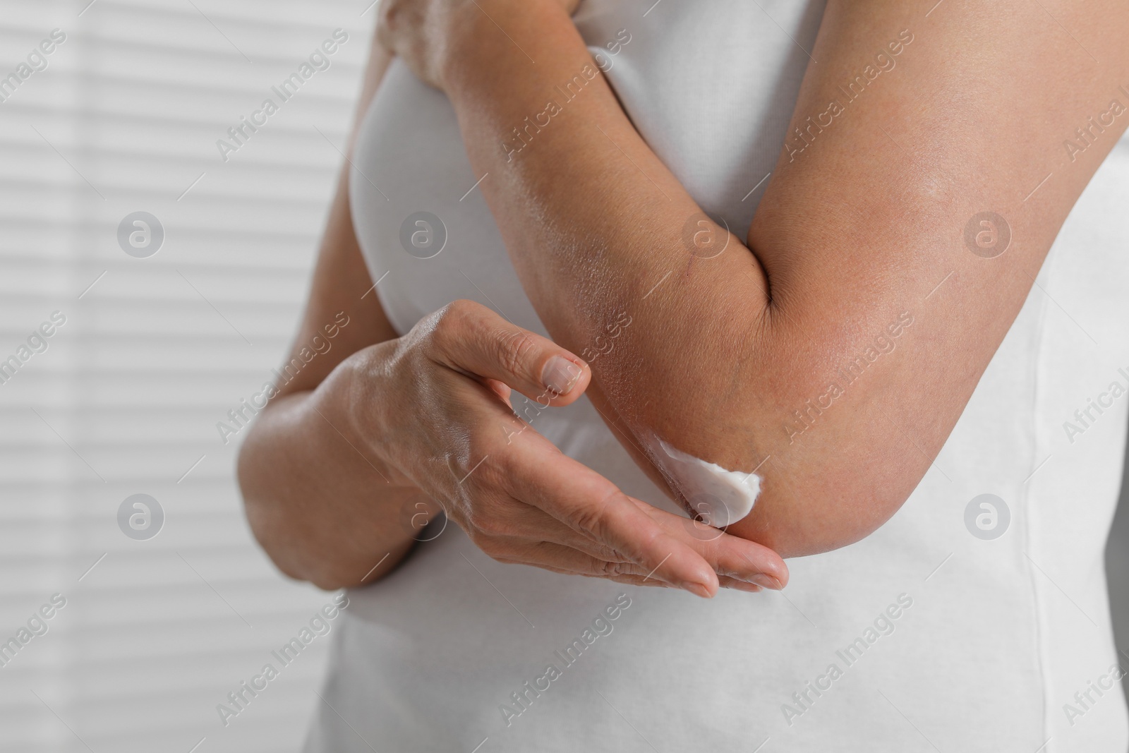 Photo of Woman applying body cream on elbow indoors, closeup