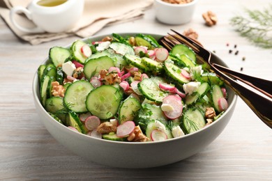 Photo of Bowl of delicious cucumber salad, spoon and fork on white wooden table, closeup