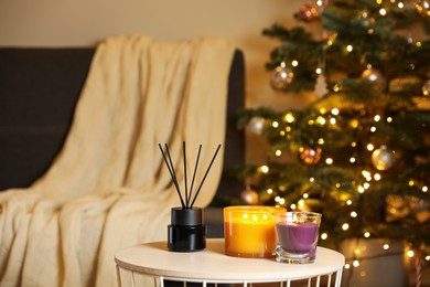 Photo of Beautiful candles and reed air freshener near Christmas tree indoors. Cosy atmosphere