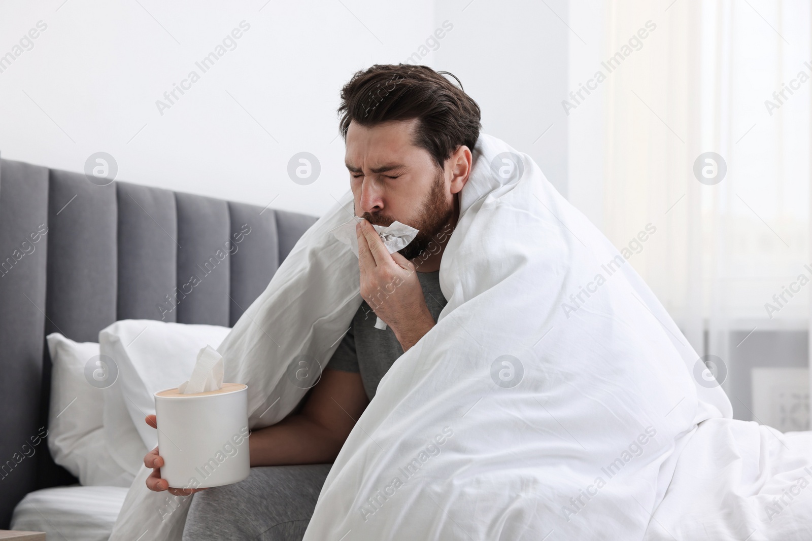 Photo of Sick man with tissue coughing on bed at home. Cold symptoms