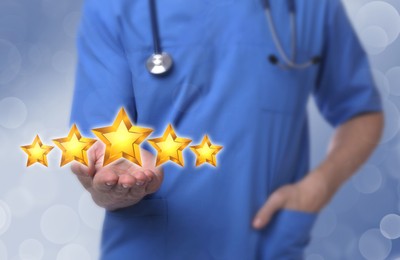 Quality evaluation. Doctor showing virtual golden stars on light blue background, closeup