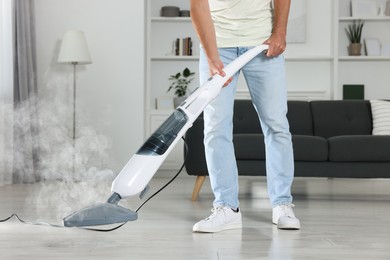 Photo of Man cleaning floor with steam mop at home, closeup