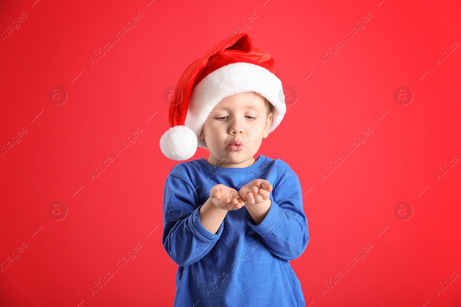 Photo of Cute little boy wearing Santa Claus hat on red background