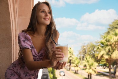 Photo of Beautiful young woman with glass of coffee standing on balcony, space for text
