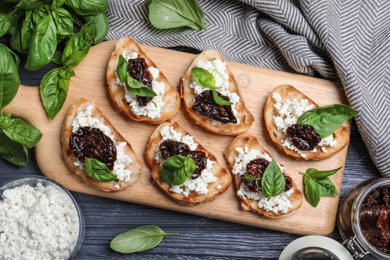 Photo of Flat lay composition of tasty bruschettas with dried tomatoes and cheese on dark grey wooden table