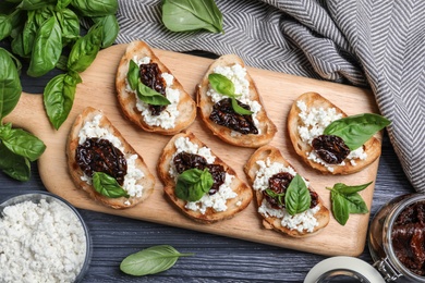 Flat lay composition of tasty bruschettas with dried tomatoes and cheese on dark grey wooden table